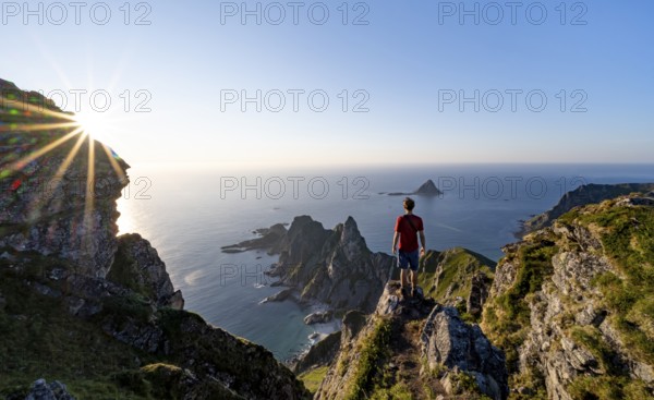 Mountaineer on the summit of Måtind or Måtinden, view of picturesque coastal landscape with sun star, rocky coast and sea, Andøya Island, Vesterålen, Nordland, Norway, Europe