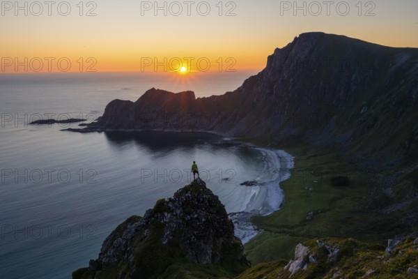 Climber on rocks in front of picturesque landscape, view of coastal landscape at sunset, cliffs and summit of Måtind or Måtinden, Høyvika beach and sea, Andøya island, Vesterålen, Nordland Norway