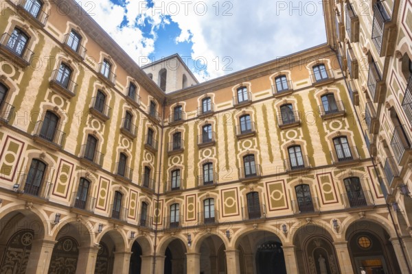 Low angle view of the courtyard of montserrat monastery, showing arched walls, balconies, and decorative facade on a sunny day
