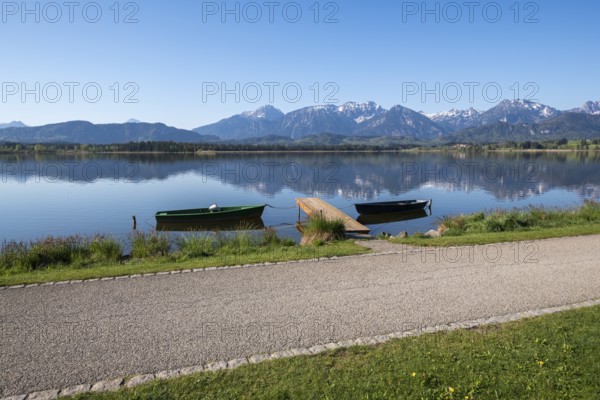 Calm lake with green and black boats, jetty and alpine landscape in the background, Hopfen am See, near Füssen, Ostallgäu district, Swabia, Bavaria, Germany, Europe