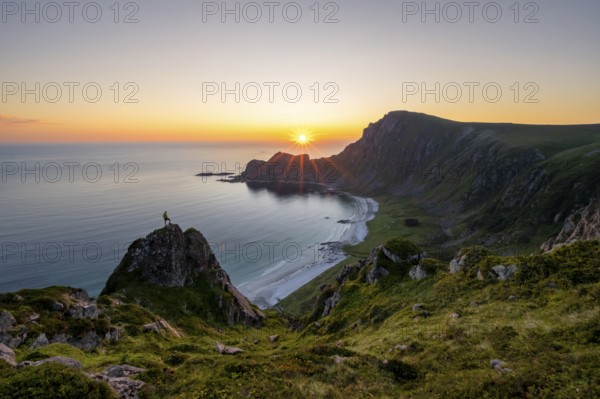 Climber on rocks in front of picturesque landscape, view of coastal landscape at sunset, cliffs and summit of Måtind or Måtinden, Høyvika beach and sea, Andøya island, Vesterålen, Nordland Norway