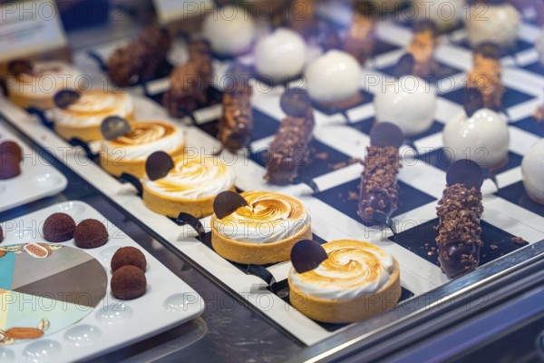 Mouth watering pastries and small cakes are neatly arranged on display in a bakery window, tempting customers with their sweet appeal