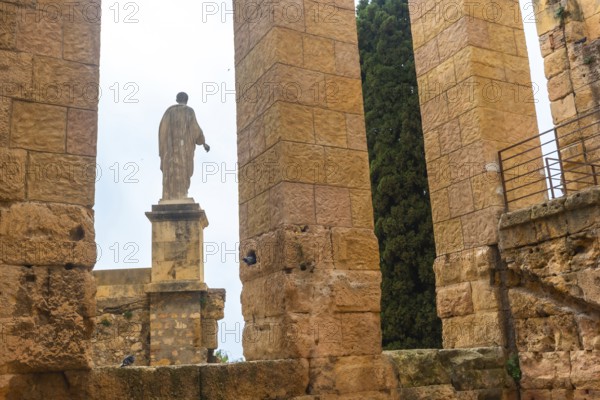 Ancient roman ruins with a statue and cypress tree in tarragona, spain, showcasing historical architecture and cultural heritage
