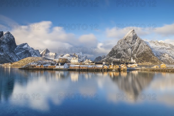 Traditional yellow rorbuer huts on the island of Sakrisøy, snow-capped mountains in the background, Sakrisoy, Reine, Lofoten, Norway, Europe