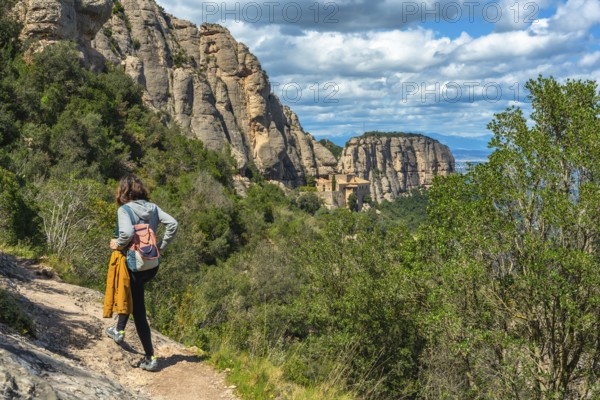 Female tourist walking on a hiking trail in montserrat mountains near barcelona with the santa maria de montserrat monastery in the background