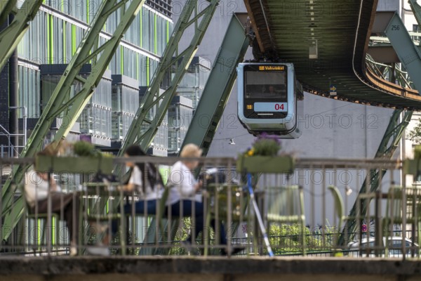 Train of the Wuppertal suspension railway runs along the Wupper, at the main station stop, terrace of Cafe23 on a small bridge over the river, North Rhine-Westphalia, Germany, Europe