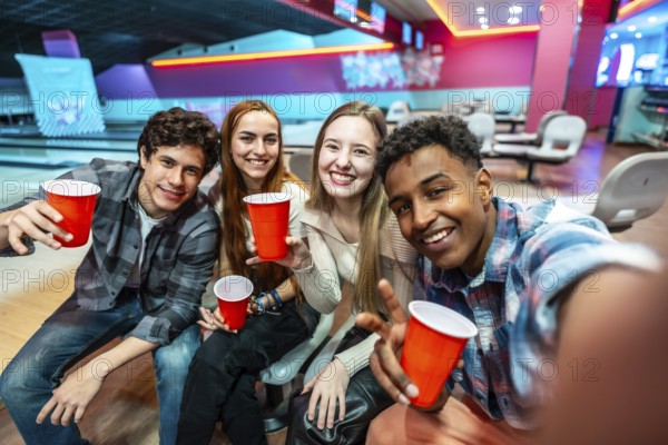 Group of cheerful young multiethnic friends taking a selfie while enjoying drinks and bowling at the alley