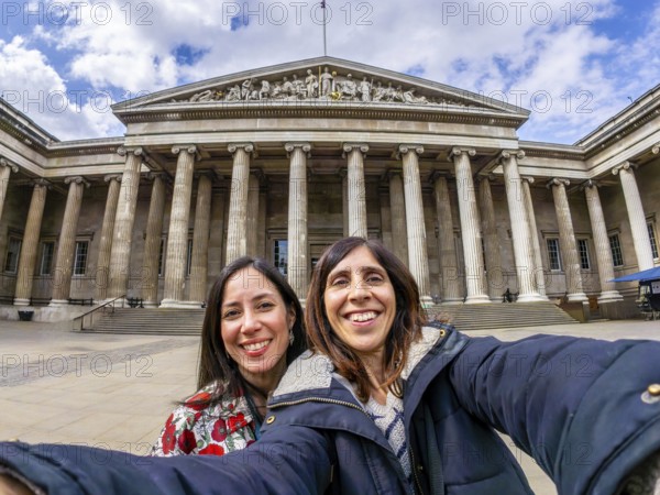 Two happy female tourists are taking a selfie with a fisheye lens in front of the british museum in london