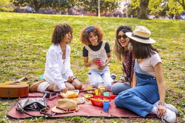 Four diverse female friends enjoying a picnic in a park, sharing food, drinks, and laughter on a sunny day