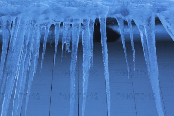 Long icicles and thick heavy ice hanging from roof edge of grey wood plank cladded building in winter, Quebec, Canada, North America