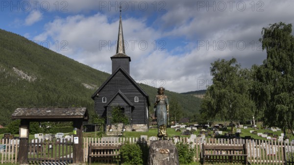 Wooden church in Sel with a cemetery and a statue of Kristian Lavranstochter, the main character from the novel of the same name by Nobel Prize winner Sigrid Undset, in front of a mountainous landscape, Olavsweg or Olavsleden, Sel municipality, Gudbrandsdalen, Norway, Europe