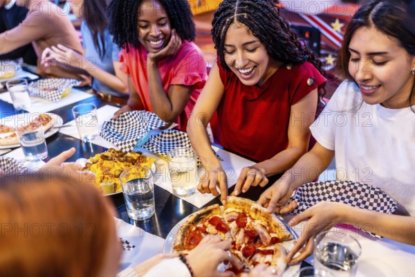 Cheerful multi ethnic friends enjoying pizza and nachos at a bowling alley restaurant, celebrating friendship and leisure time together