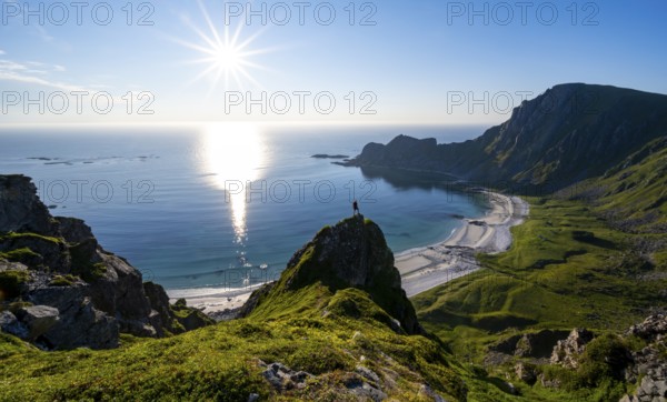 Climber on a rock, view of picturesque coastal landscape with sun star, steep coast with peak Måtind or Måtinden, Høyvika beach and sea, hike to the summit of Måtind, Andøya island, Vesterålen, Nordland, Norway, Europe