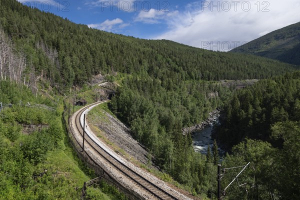 Railway tracks run through a wooded, mountainous landscape next to the river Gudbrandsdalslågen, Dovrebanen, near Sel, Gudbrandsdalen, Norway, Europe