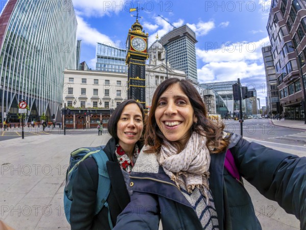 Two happy tourists taking a selfie with a fisheye lens in front of a historic clock tower in london, uk, capturing their travel adventure