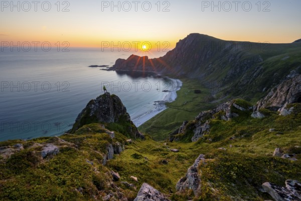 Climber on rocks in front of picturesque landscape, view of coastal landscape at sunset, cliffs and summit of Måtind or Måtinden, Høyvika beach and sea, Andøya island, Vesterålen, Nordland Norway