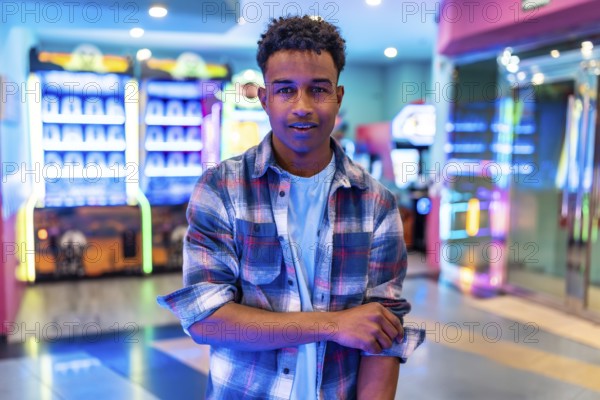 Young man standing in a vibrant arcade, surrounded by colorful lights and gaming machines, enjoying his weekend leisure time