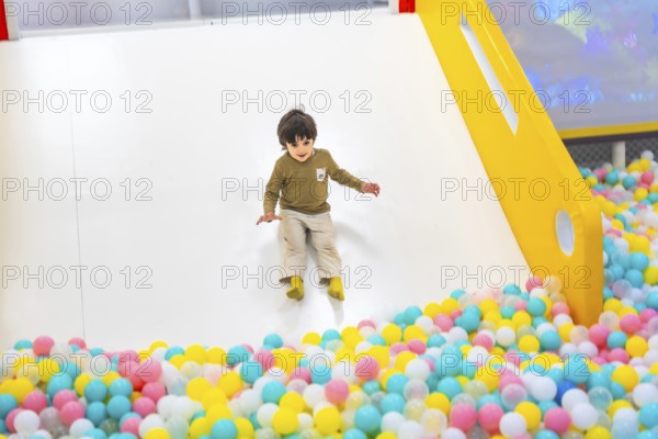 Young boy joyfully sliding into a vibrant, colorful ball pit at an indoor playground, surrounded by cheerful plastic balls and laughter