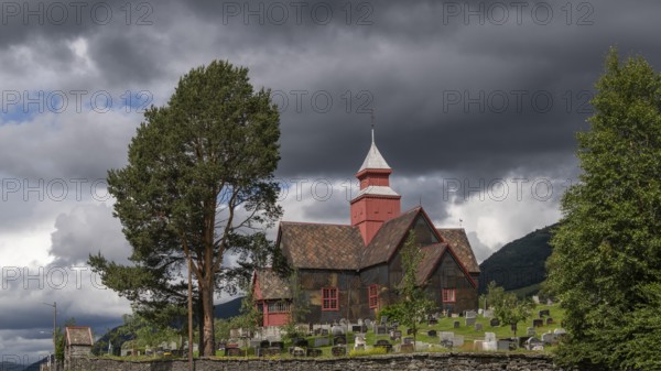 Historic church with cemetery under dark clouds and a tree in the foreground, Dovre, Fylke Innlandet, upper Gudbrandsdalen, Norway, Europe