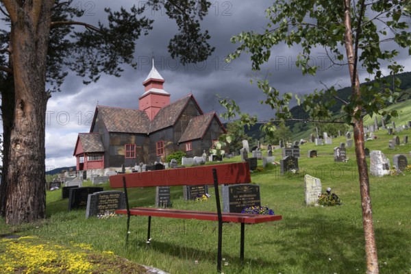 Red bench in front of church and cemetery under a gloomy sky, Dovre church, Dovre kyrkje, Dovre, Fylke Innlandet, upper Gudbrandsdalen, Norway, Europe