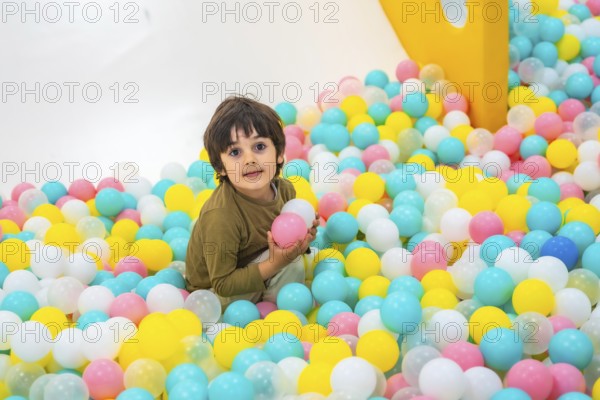 Young boy enjoying playtime in a vibrant ball pit, surrounded by colorful plastic balls in a lively indoor play area