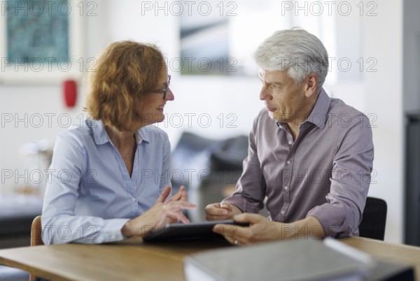 Symbolic photo. A woman and a man sit together at a table with a tablet and talk. Berlin, 13.08.2024