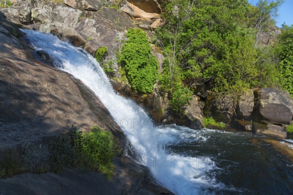 A small waterfall flows over large rocks, surrounded by green plants under a sunny sky, Cascada del Diablo, Devil's Waterfall, Garganta de Gualtaminos, Gualtaminos Gorge, La Vera, Cáceres, Caceres, Extremadura, Spain, Europe