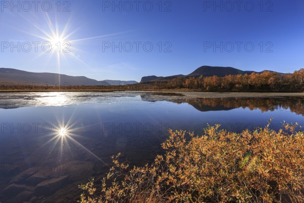 Mountains reflected in lake, autumn colours, sun, sun star, bright, friendly, Nikkaluokta, Laponia, Lapland, Sweden, Europe