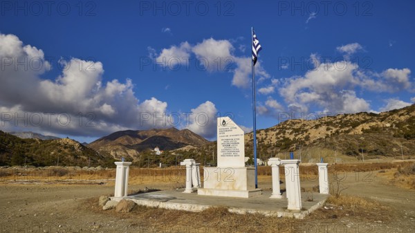 White memorial with Greek flag against a clear blue sky and mountain backdrop, Christopher Litos Monument, Pigadia, town and harbour, Pigadia Bay, main town, Karpathos, Dodecanese, Greek Islands, Greece, Europe
