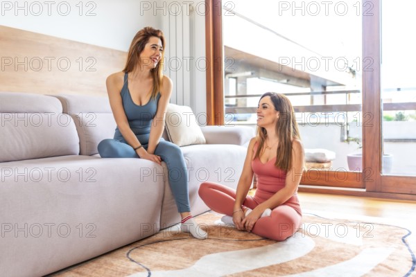 Two friends practicing yoga and meditation in a bright living room, enjoying an online class together for relaxation and wellness