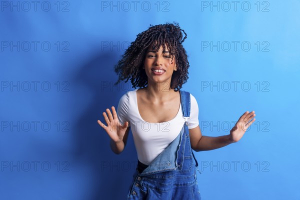 Young woman with curly hair dancing joyfully against a vibrant blue backdrop, embodying carefree energy and youthful expression in a studio setting