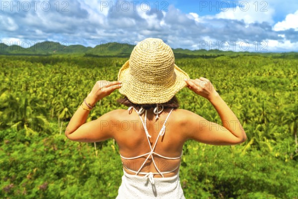 Young woman enjoying the view of a wide coconut plantation in siargao island, philippines, holding her straw hat