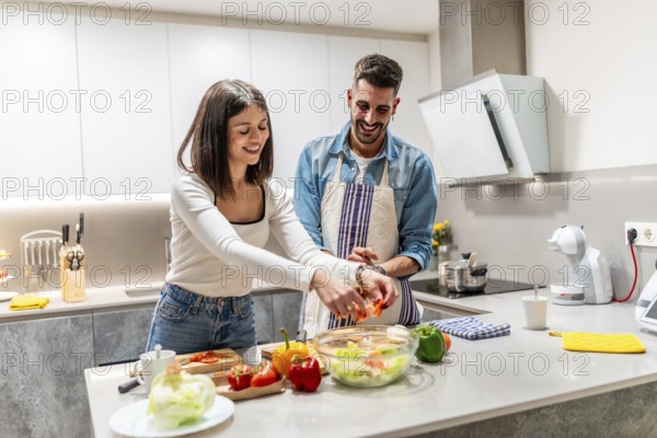 Cheerful couple smiling and preparing a healthy salad together in a modern kitchen, enjoying their quality time