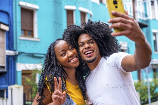 African couple gesturing success taking a selfie in a colorful street