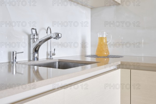 A contemporary kitchen features a polished stone countertop with a shiny faucet and a glass pitcher filled with a refreshing drink. The clean lines and light colours create a bright atmosphere