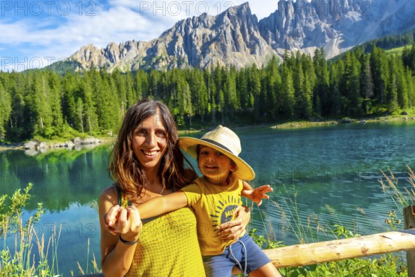 Mother and son smiling and enjoying summer holidays at lake carezza with the latemar mountain range in the background