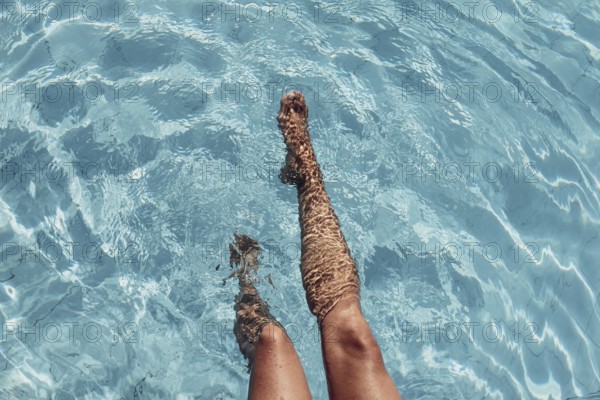 Women's legs in the water of a pool with turquoise water and summer light
