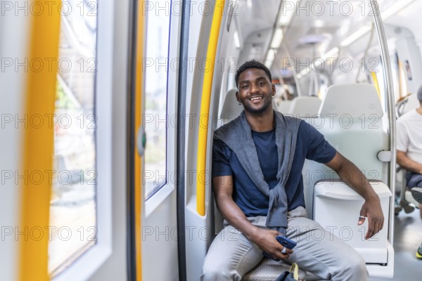 Portrait of a handsome african young man smiling at camera while sitting on the public metro commuting