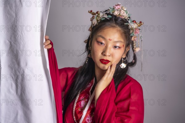 A woman in a red dress with a flower headpiece is posing for a photo. The image has a traditional and elegant feel to it, with the woman's red dress