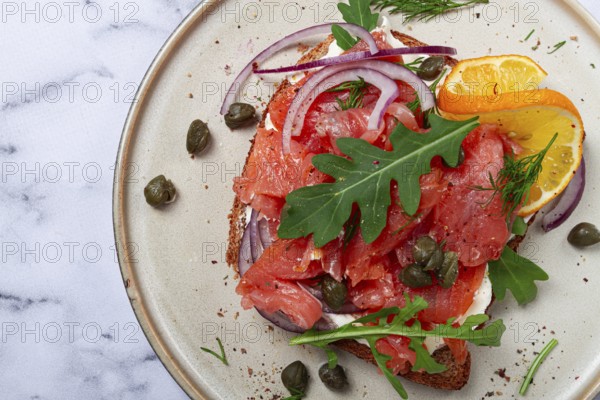 Sandwich with freshly smoked salmon, on black bread, with cottage cheese, with herbs and red onions, capers and pieces of citrus fruits, on a marble countertop, breakfast, no people