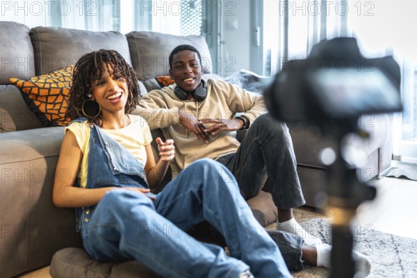 Two young content creators are recording a video blog from their living room, discussing and gesturing towards the camera