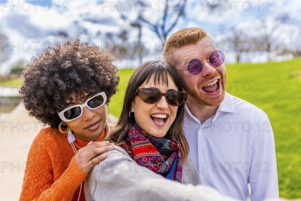 Three cheerful multi ethnic friends are taking a selfie in a park, laughing and enjoying a beautiful sunny day together