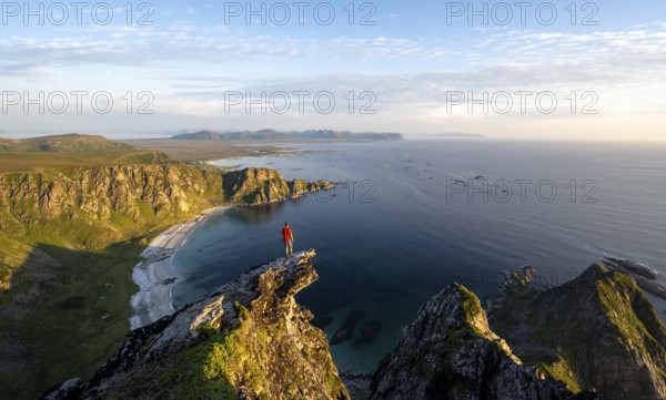 Evening mood, mountaineer standing on a rocky outcrop on the summit of Måtind, view of coastal landscape, Høyvika beach and sea, Måtinden, Andøya island, Vesterålen, Nordland Norway
