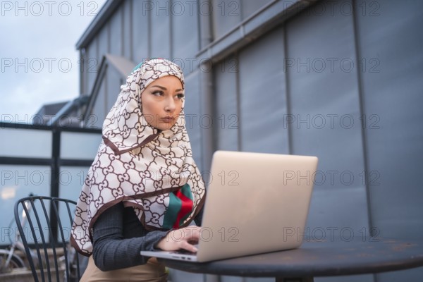Arab girl with a white veil at the computer on the terrace of a coffe shop, contrabass with the computer. Modern Arab young man with new technologies