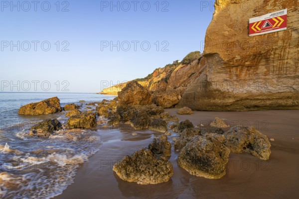 ROCKFALL UNSTABLE CLIFFS, KEEP A SAFE DISTANCE is written in English on a warning sign in Portugal on the cliffs of the Atlantic Ocean. Rocks and stones break out here again and again and injure people., Albufeira, Faro, Portugal, Europe