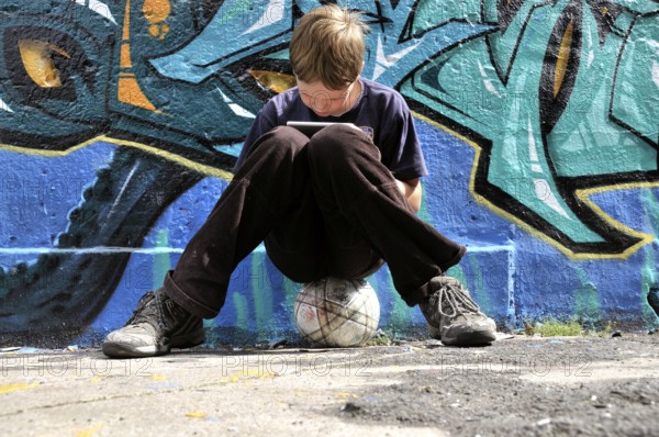 Ten-year-old boy playing with his Nintendo in front of a graffiti wall, football pitch, Germany, Europe
