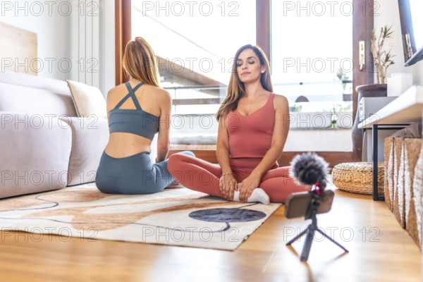 Two women recording an online yoga and meditation class in a cozy living room, embracing wellness and connection through digital content creation