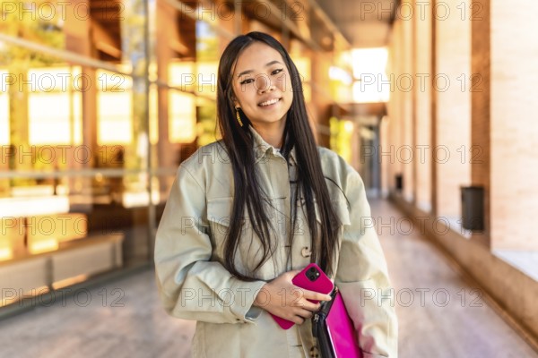 Portrait of a female beauty chinese cute university student standing with mobile phone and laptop