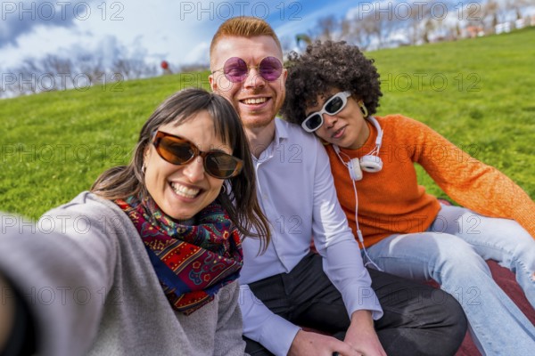 Three cheerful friends are taking a selfie in a park, enjoying a sunny spring day together