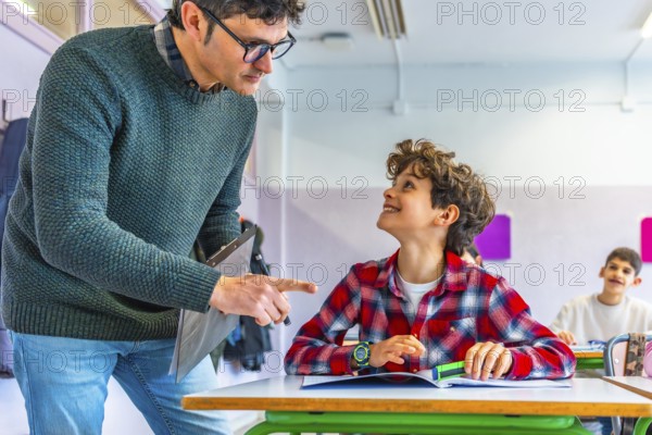 Elementary school teacher engaging with a smiling student while explaining a lesson at their desk in a cheerful classroom setting